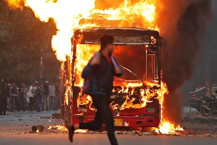 Seorang demonstran melintas didepan bus yang dibakar pengunjuk rasa menentang UU anti muslim di India.