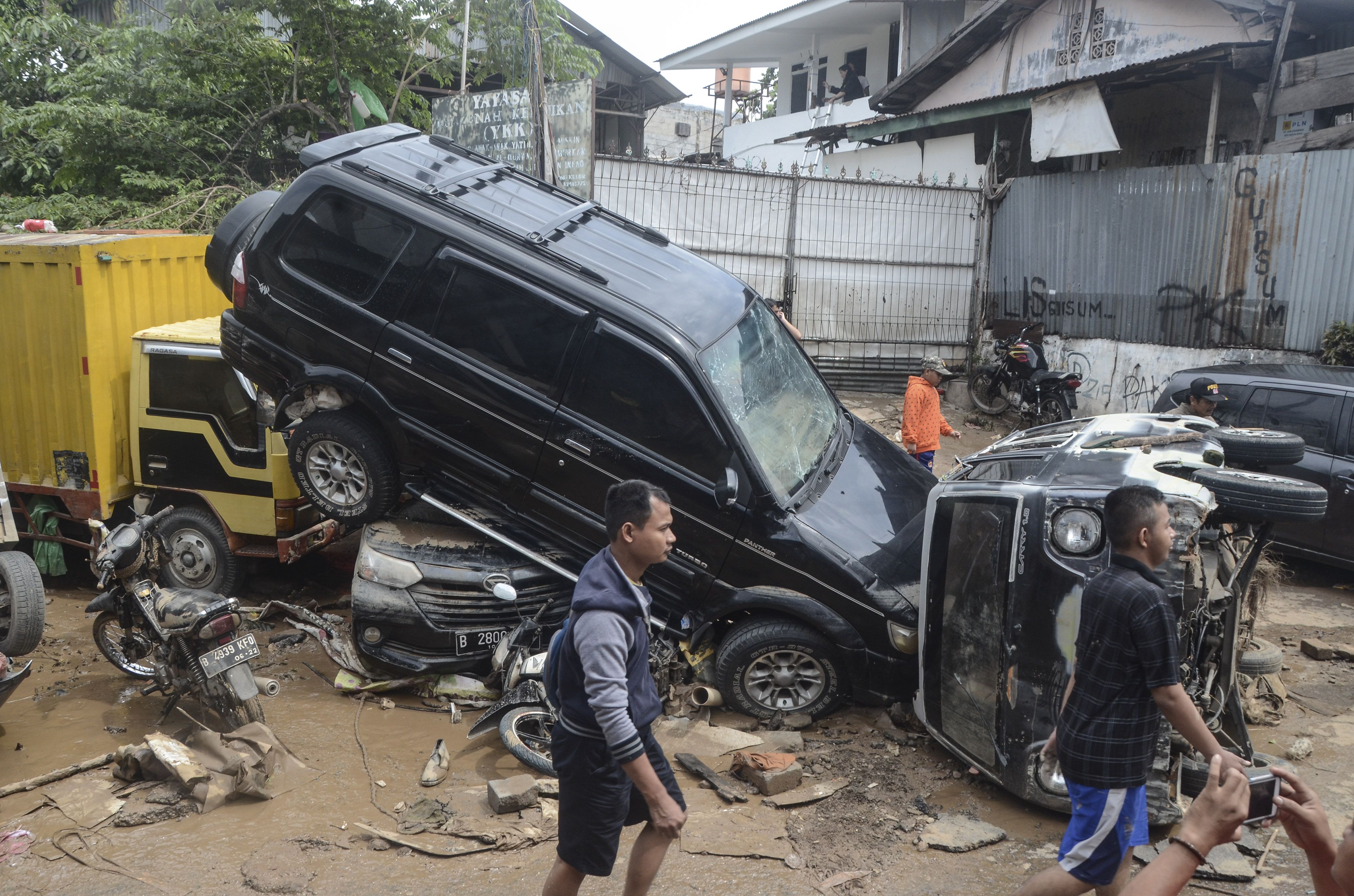Sejumlah warga berjalan di dekat mobil yang rusak pascabanjir di Perumahan Pondok Gede Permai Bekasi, Jawa Barat, Kamis (2/1/2020). Banjir yang telah menggenangi rumah warga selama dua hari tersebut terjadi akibat luapan Kali Bekasi. ANTARA FOTO/ Fakhri Hermansyah/wsj.