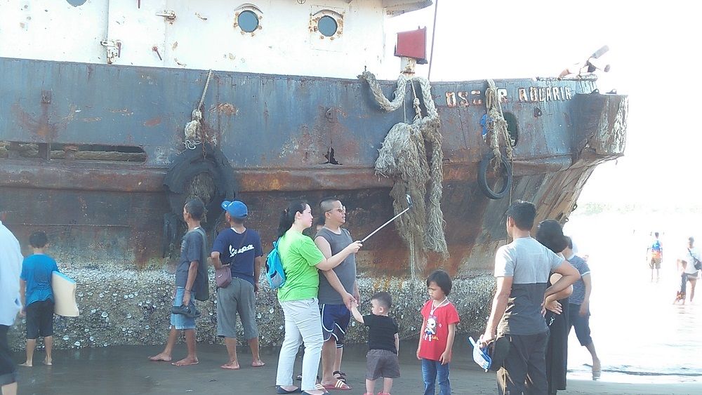 WISATAWAN berfoto dengan latar belakang Tugboat Oscar Aquaria di Pantai Barat Pangandaran, Minggu 19 Januari 2020.*
