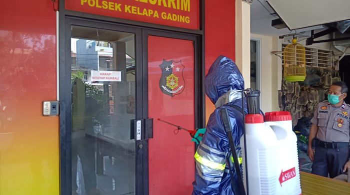 Anggota Kepolisian Polsek Kelapa Gading tengah menyemrotkan disinfektan menggunakan jas hujan.*