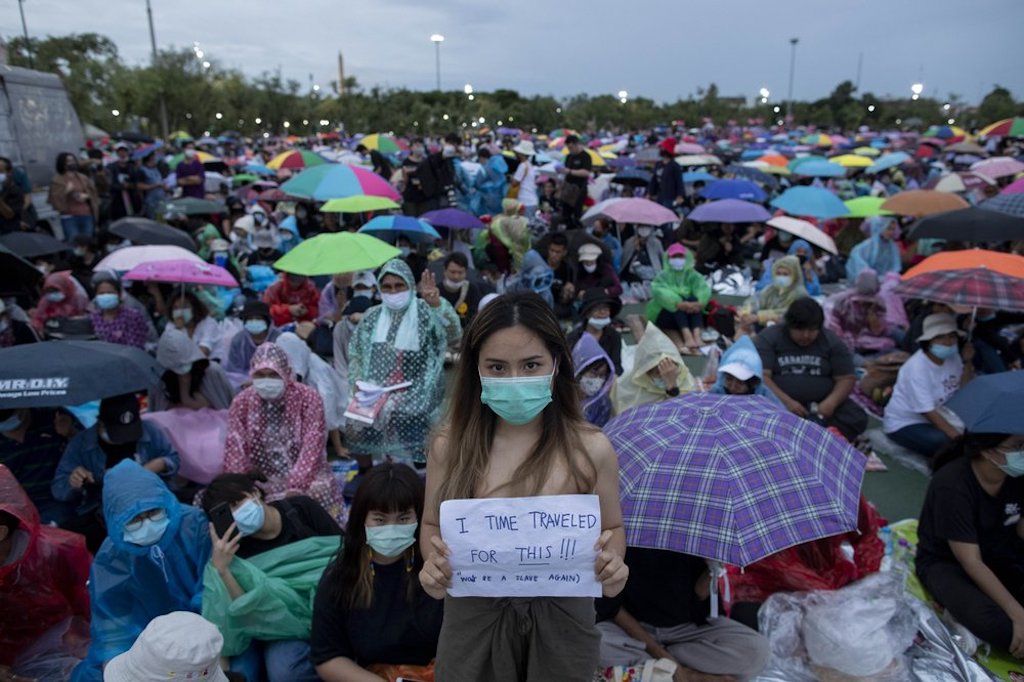 Seorang pengunjuk rasa pro-demokrasi menampilkan plakat saat rapat umum di Sanam Luang dengan The Grand Palace menyala di latar belakang di Bangkok, Thailand, Sabtu, 19 September 2020. 