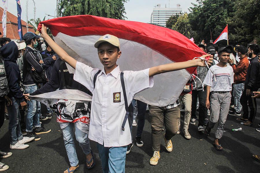Remaja bepaikaian SMA membawa bendera Merah Putih saat demo tolak Omnibus Law Undang - Undang Cipta Kerja 