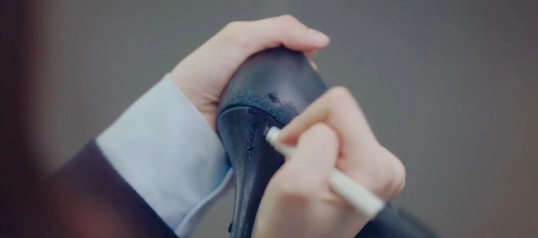 Adegan Suzy mewarnai tumit sepatu dengan spidol hitam.