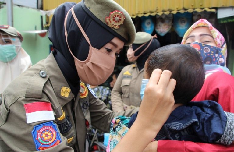 Anggota Satpol PP Kota Bandung memasangkan masker ke anak-anak.