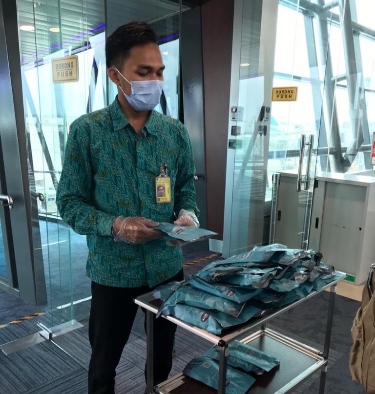 Petugas memberikan hand sanitizer dan masker kepada penumpang yang akan memasuki pesawat