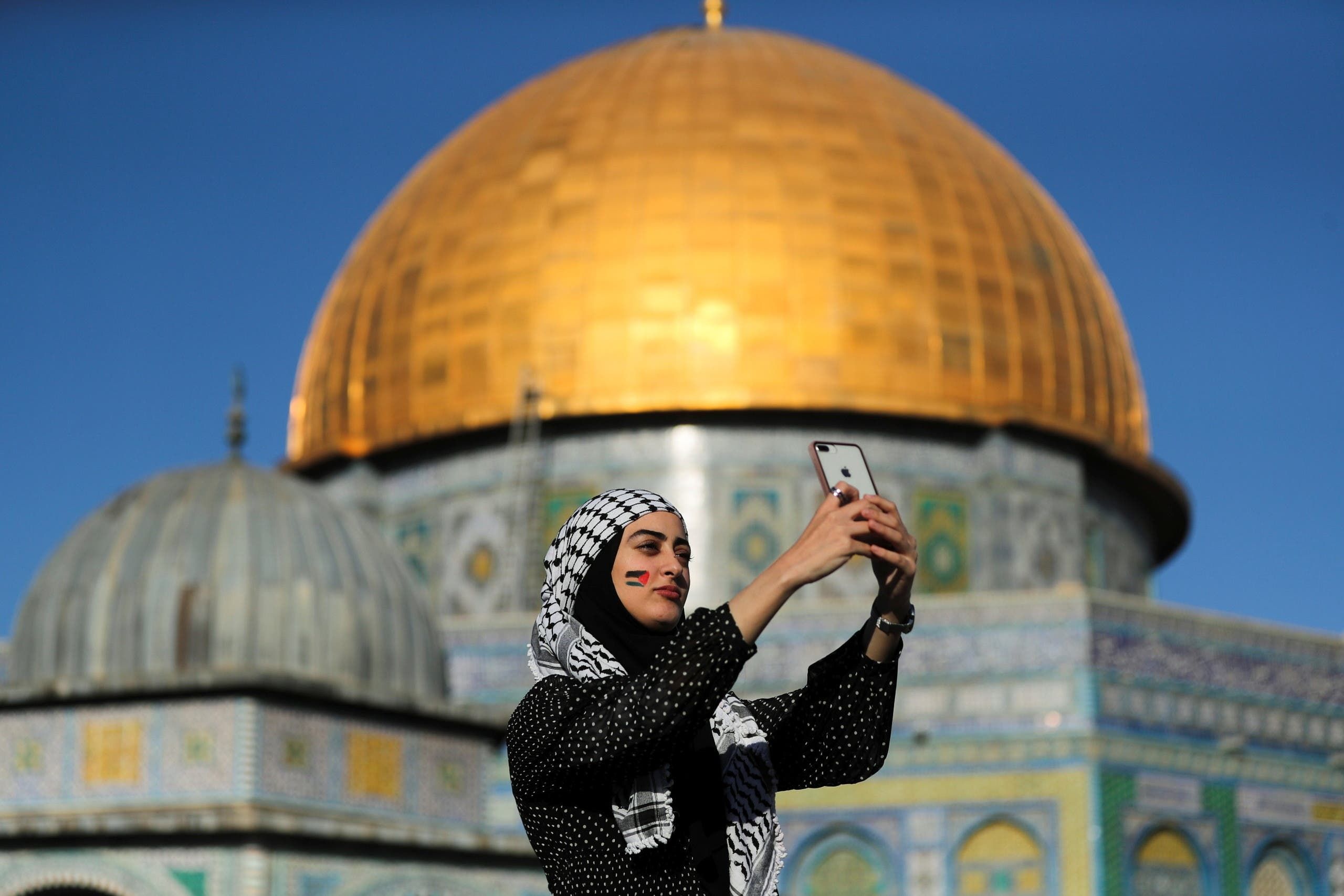 Seorang wanita Palestina mengambil foto selfie saat Kubah Batu terlihat di latar belakang, saat shalat Idul Fitri pada 13 Mei 2021/Reuters