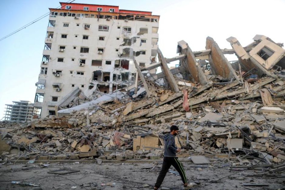 Potret bangunan yang hancur akibat serangan udara oleh Israel dan dilewati seorang laki-laki Palestina di Kota Gaza/Reuters/Suhaib Salem