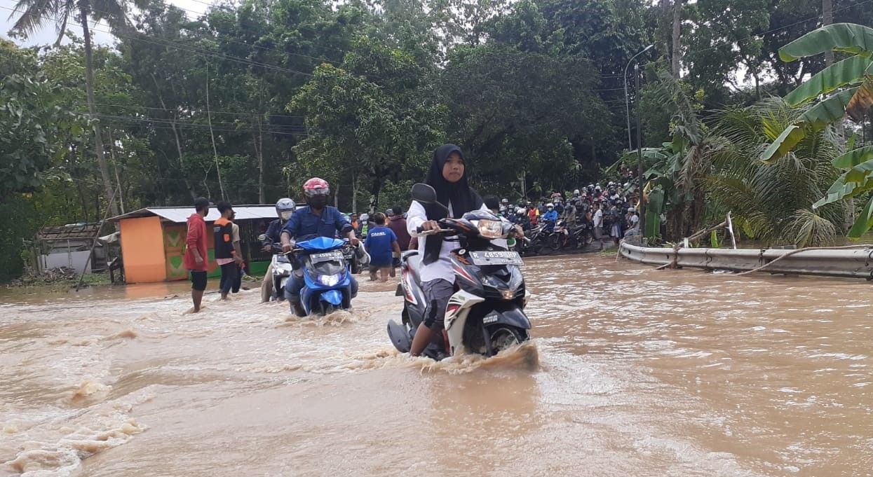 Warga melintasi genangan air di jalan raya Jeruklegi-Kawunganten. Jalan tersebut sempat putus, tidak bisa dilewati