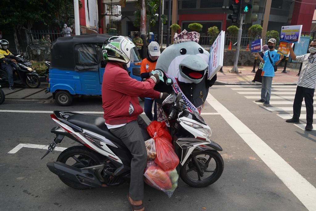 kegiatan sosialasasi dilakukan dengan membagikan masker oleh maskot Konsumen Berdaya si Enda kepada para pengendara motor dan mobil yang berhenti di lampu merah pada Selasa, 3 Agustus 2021.