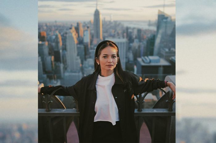 Enzy Storia tampil dengan gaya casual dan berfoto dengan latar belakang Empire State Building di New York.