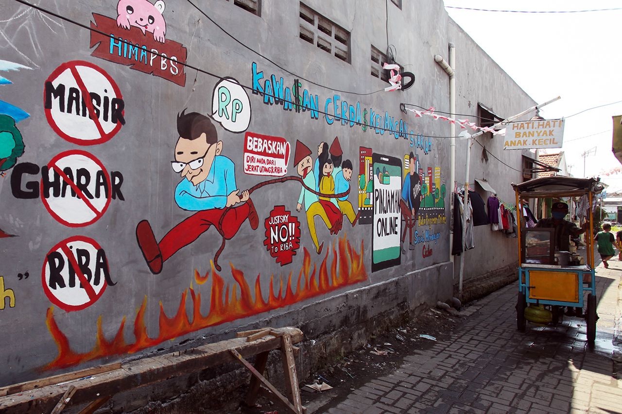 Penjual makanan melintas di dekat dinding bermural di kawasan Tempurejo, Surabaya, Jawa Timur, Selasa (7/9/2021). Mural tersebut sebagai sarana imbauan kepada masyarakat terhadap bahaya pinjaman daring atau 'online' (pinjol) ilegal yang sekarang lagi marak. 