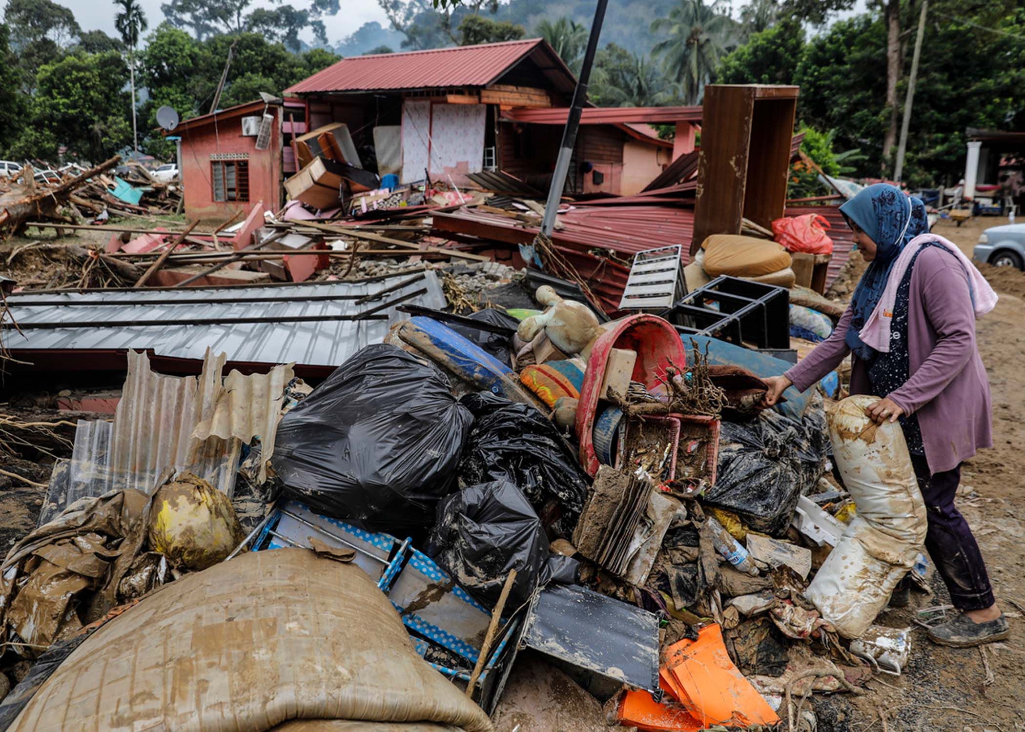Seorang wanita mengumpulkan puing-puing di Hulu Langat, Malaysia, pada 22 Desember 2021. Ada tekanan publik pada pemerintah untuk mengizinkan korban banjir menarik tabungan dari rekening Dana Penyedia Karyawan mereka. 