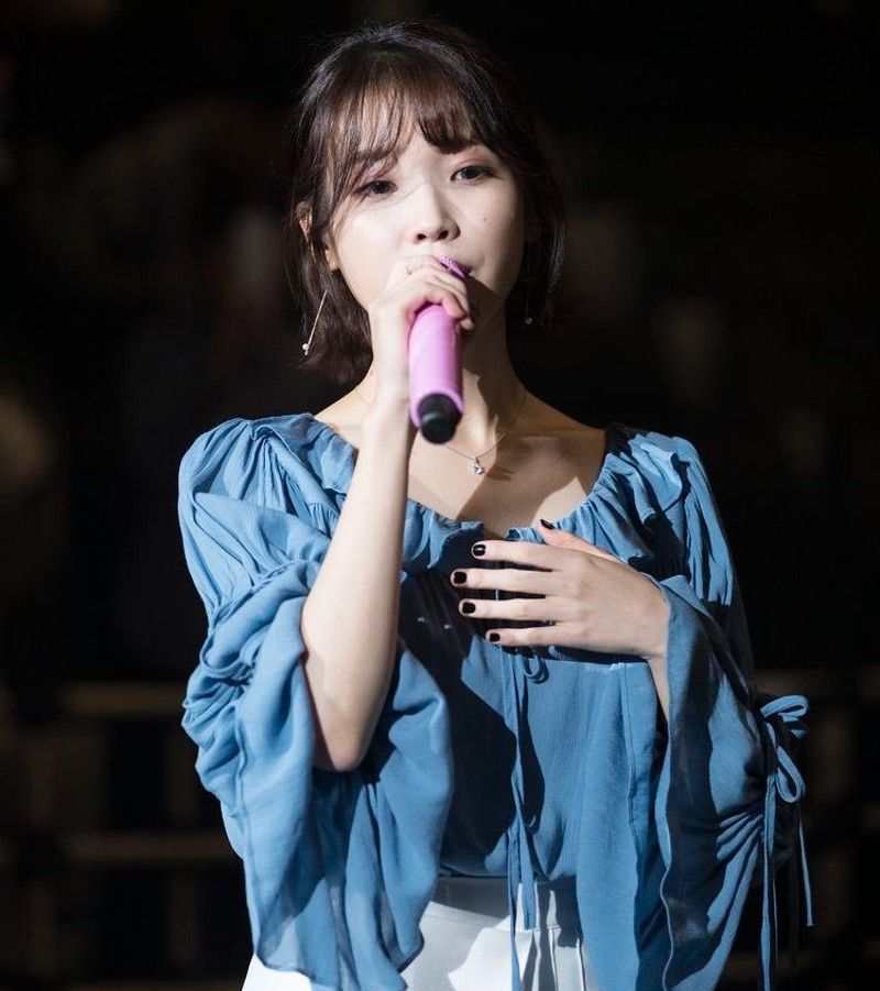IU saat tampil di atas panggung dengan baju berwarna biru dan rok putihnya