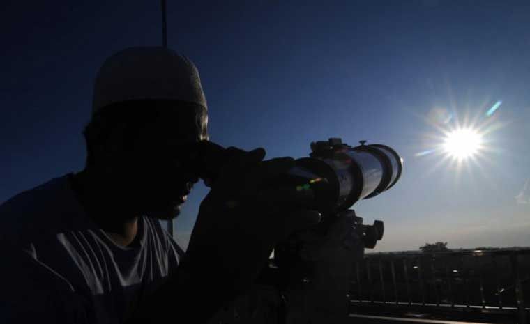 Ilustrasi seorang petugas sedang menggunakan teleskop untuk melihat hilal.