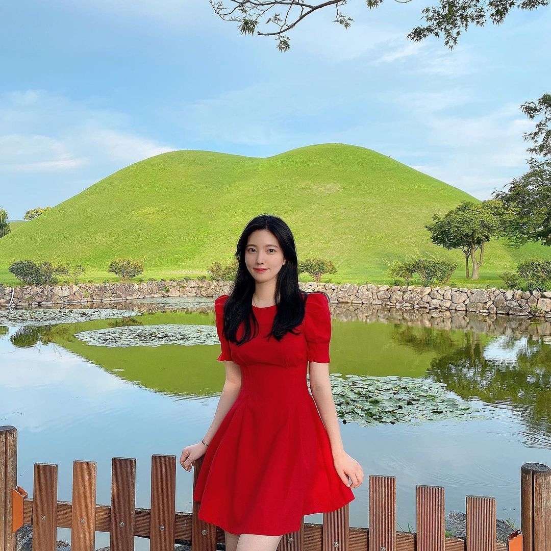 Lee Eun Jin terlihat menawan mengenakan gaun merah dengan pemandangan alam yang indah.