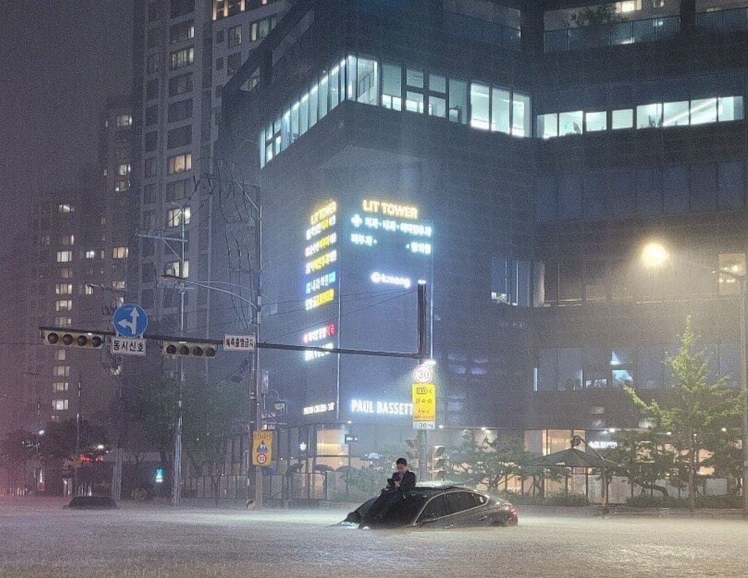 Seorang pria tampak duduk santai di atas sebuah mobil yang nyaris tenggelam