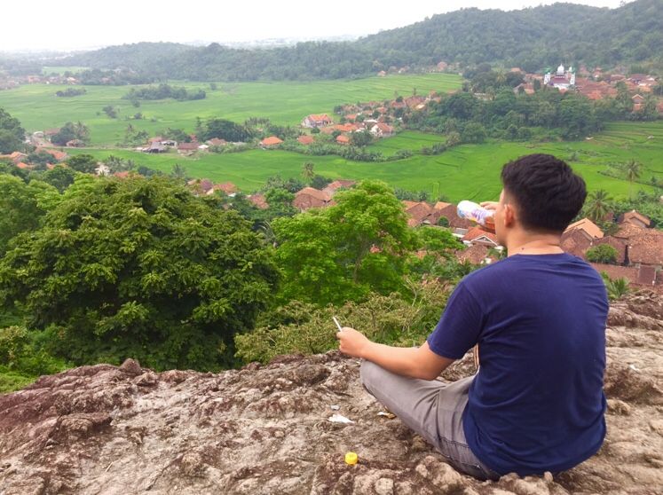 Potret seseorang sedang menikmati panorama sawah dan bukit hijau di atas bukit Batu Gede Sayar, wisata alam hidden gem di Serang Banten / Ahmed Furqon / Kabar Banten