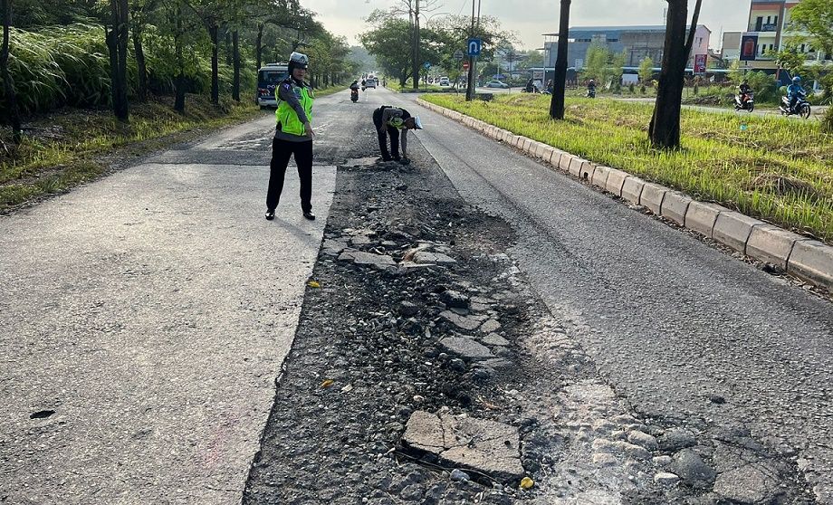 Dua polisi memperlihatkan jalan Mukakuning - Tanjungpiayu, jalan Provinsi Kepri di Batam yang rusak.