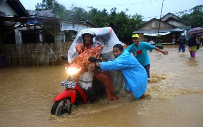 Warga membantu pengendara sepeda motor melintasi jalan yang terendam banjir di Desa Bulayak, Kabupaten Hulu Sungai Tengah, Provinsi Kalimantan Selatan, Kamis 16 Maret 2023. 