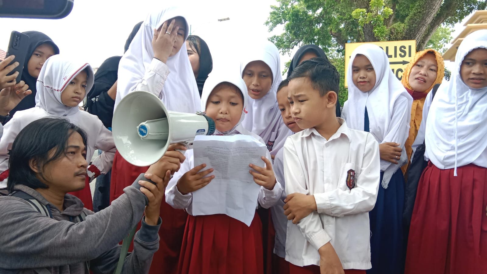 Aksi anak Sekolah Dasar membacakan peraturan terkait izin perkebunan kelapa sawit, yang dibacakan di depan Mapolda Jambi, Senin, 10 April 2023.