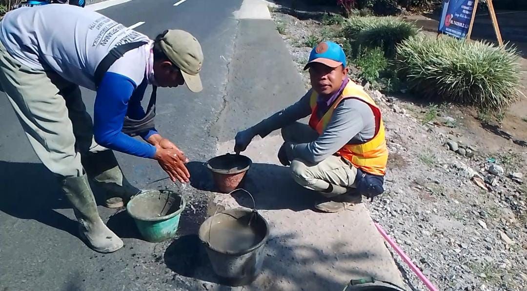 Dua pekerja tampak tengah melapisi cor beton bahu jalan Jalur Liwa, Lampung Barat-Ranau OKU Selatan dengan aci semen di salah satu titik di Pemangku Pekon Balak, Padang Cahya, Balik Bukit.