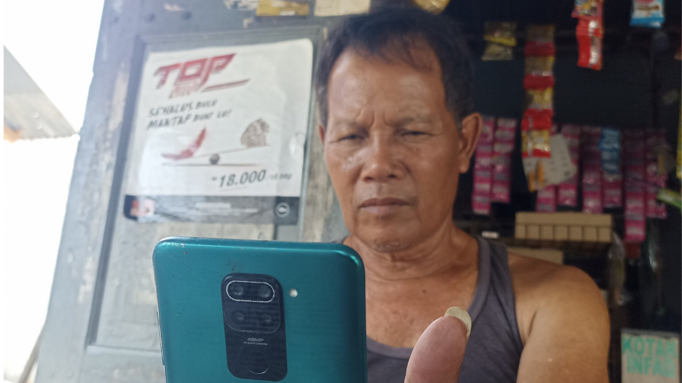Seorang pedagang warung kelontong memanfaatkan Smartphone untuk mengakses aplikasi BRI Mobile dalam bertransaksi