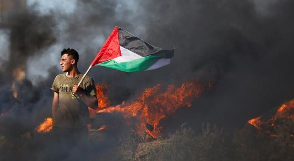 Seorang warga Palestina mengibarkan bendera saat mengikuti protes menentang serangan tentara Israel di Jenin, di sepanjang pagar perbatasan Israel-Gaza di timur Kota Gaza, 3 Juli 2023. (REUTERS/Mohammed Salem)