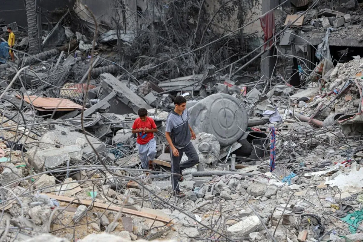 Orang-orang berjalan di antara puing bangunan yang hancur akibat serangan udara Israel di kota Khan Younis di Jalur Gaza selatan, Jumat 27 Oktober 2023. 