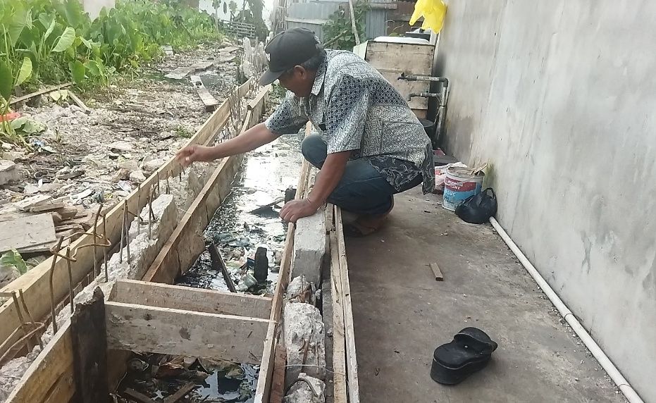 Nasuki, warga setempat saat mencoba mengecek kekuatan turap beton untuk saluran yang dibangun tepat dibelakang rumahnya