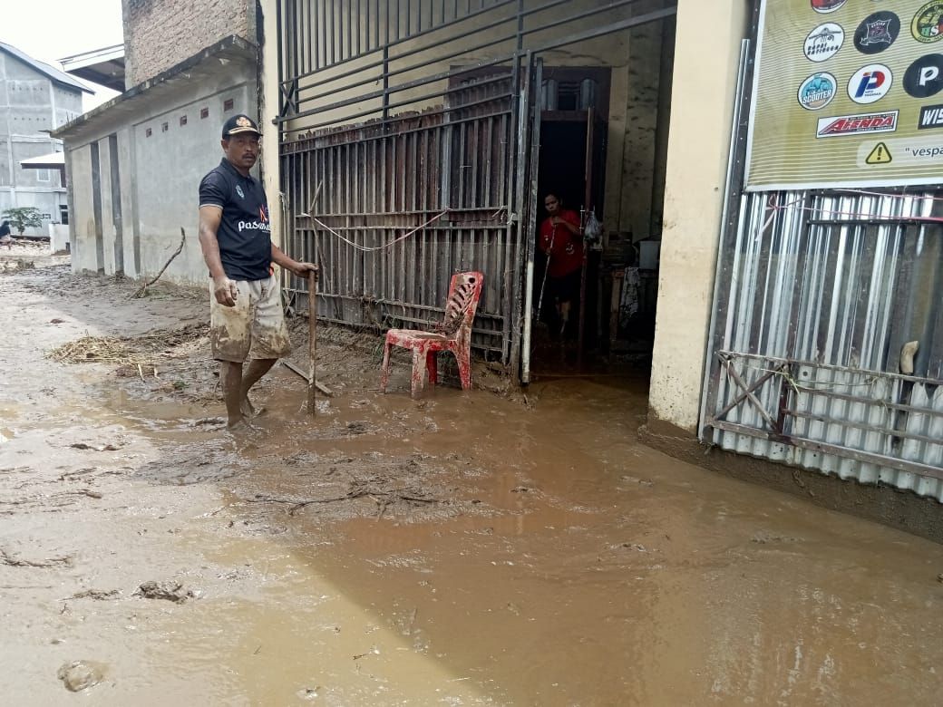 Salah seorang warga korban banjir tengah berupaya membersihkan rumahnya dari lumpur