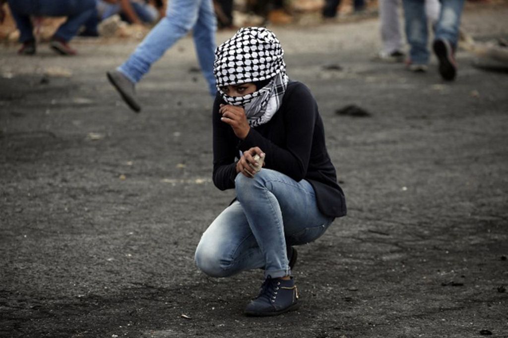 Seorang perempuan muda Palestina berjongkok mengamati pergerakan serdadu Zionis sebelum melemparkan batu//Foto: Abed Al Hashlamoun - EPA 