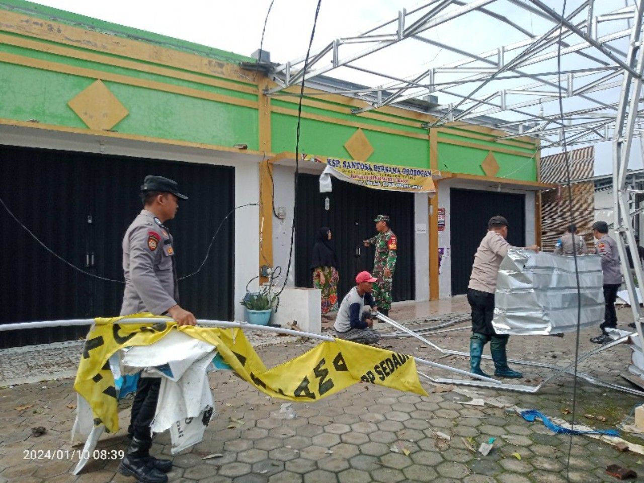 Aparat TNI Polri melakukan kerja bakti membenahi atap yang rusak pada bangunan toko.