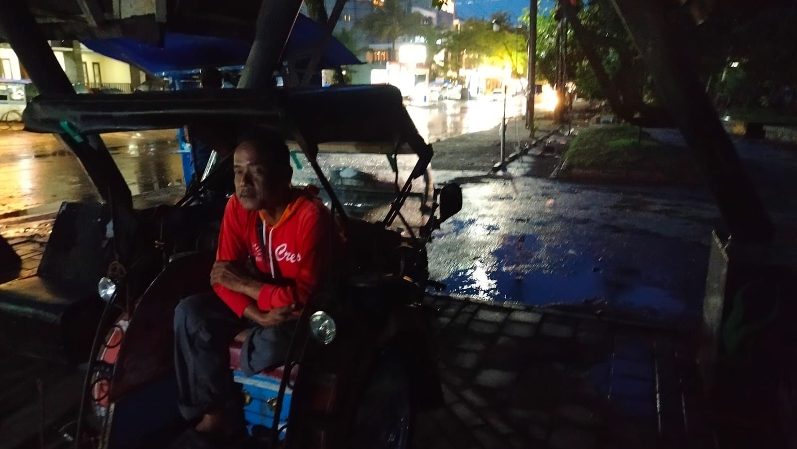 Salah seorang pekerja jasa angkut wisata Pantai Pangandaran Jumono, berteduh saat hujan melanda Kamis 18 Januari 2024*/Kabar Priangan/Kiki Masduki 