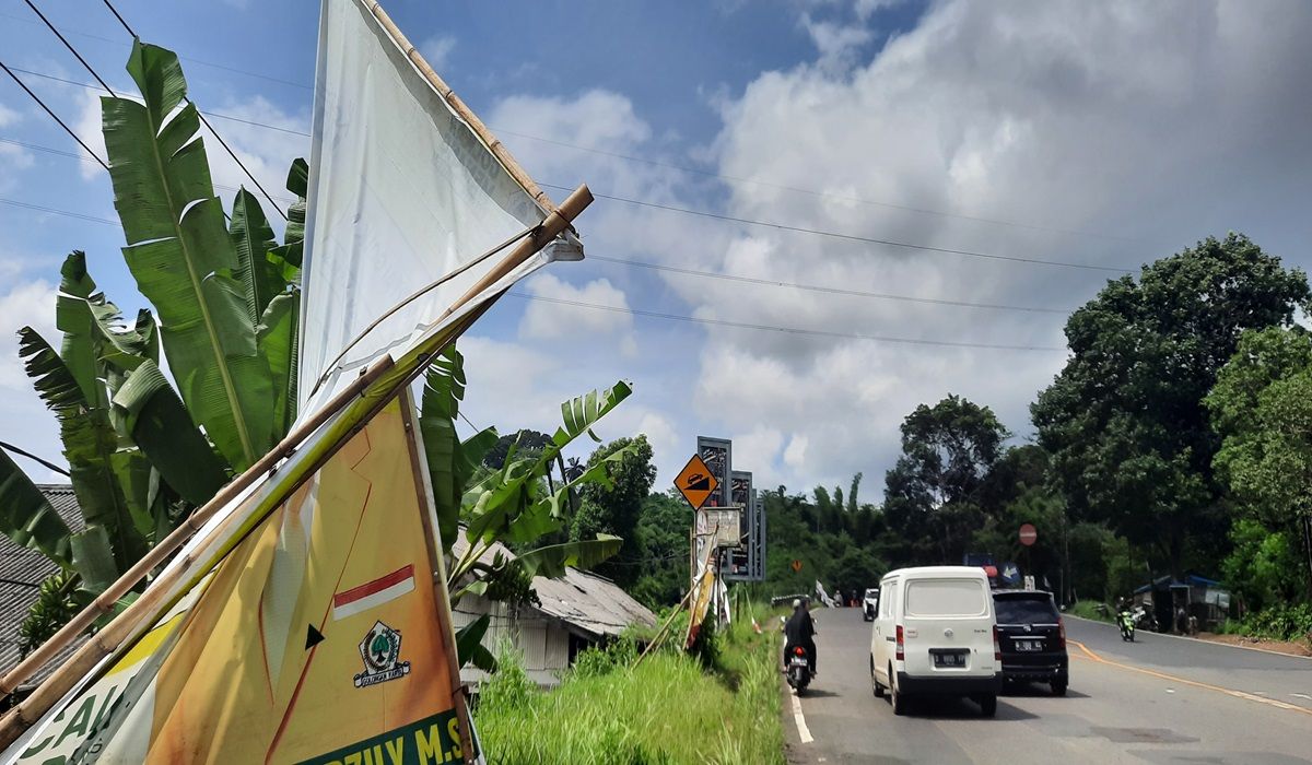 Pengendara melintasi alat peraga kampanye Pemilu 2024 yang nyaris ambruk di tepi jalan, kawasan  Sirnaraja, Desa Mandalasari, Kecamatan Cikalongwetan, Kabupaten Bandung Barat.