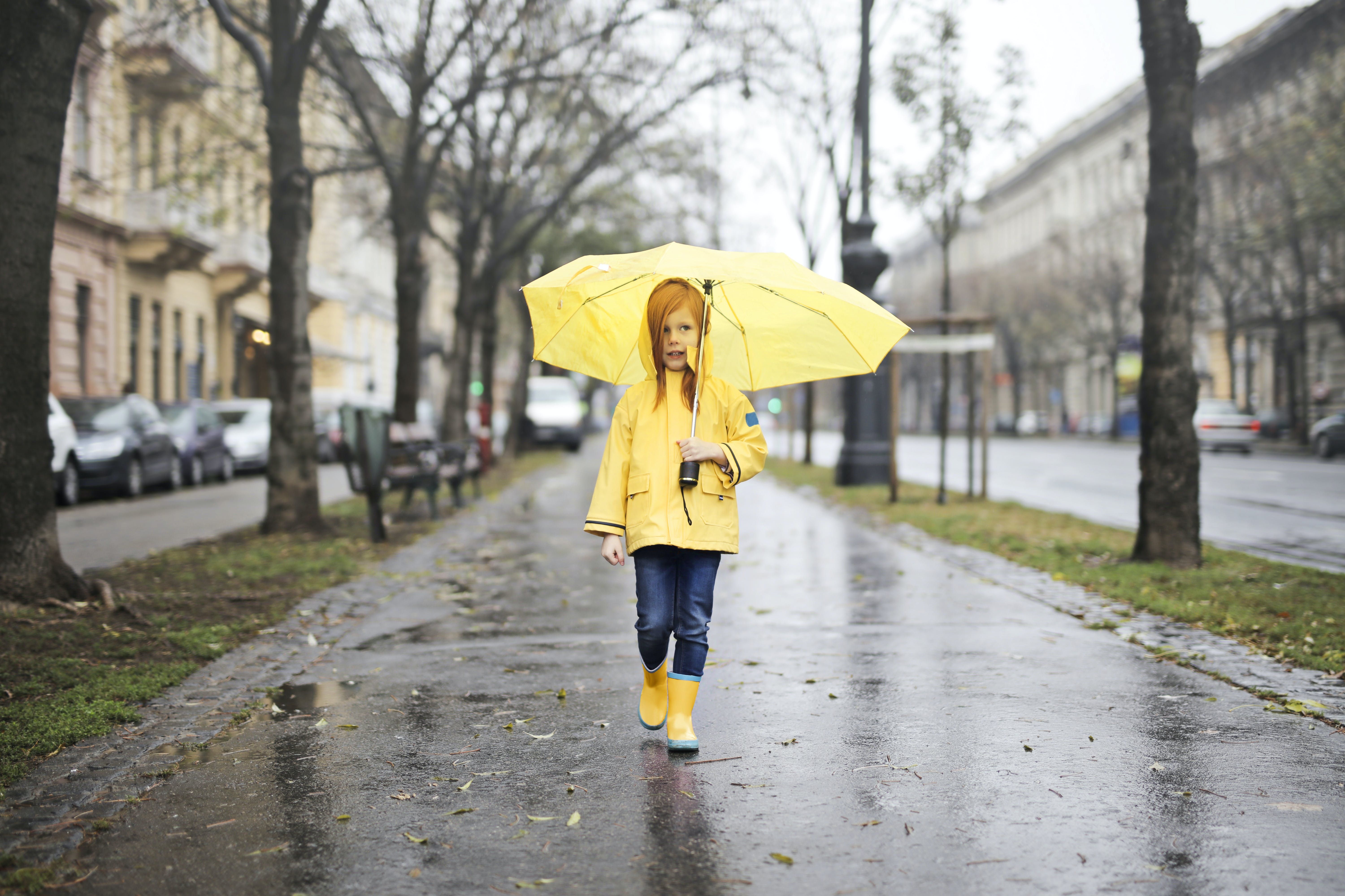 Ilustrasi seorang anak di bawah hujan dengan payung.