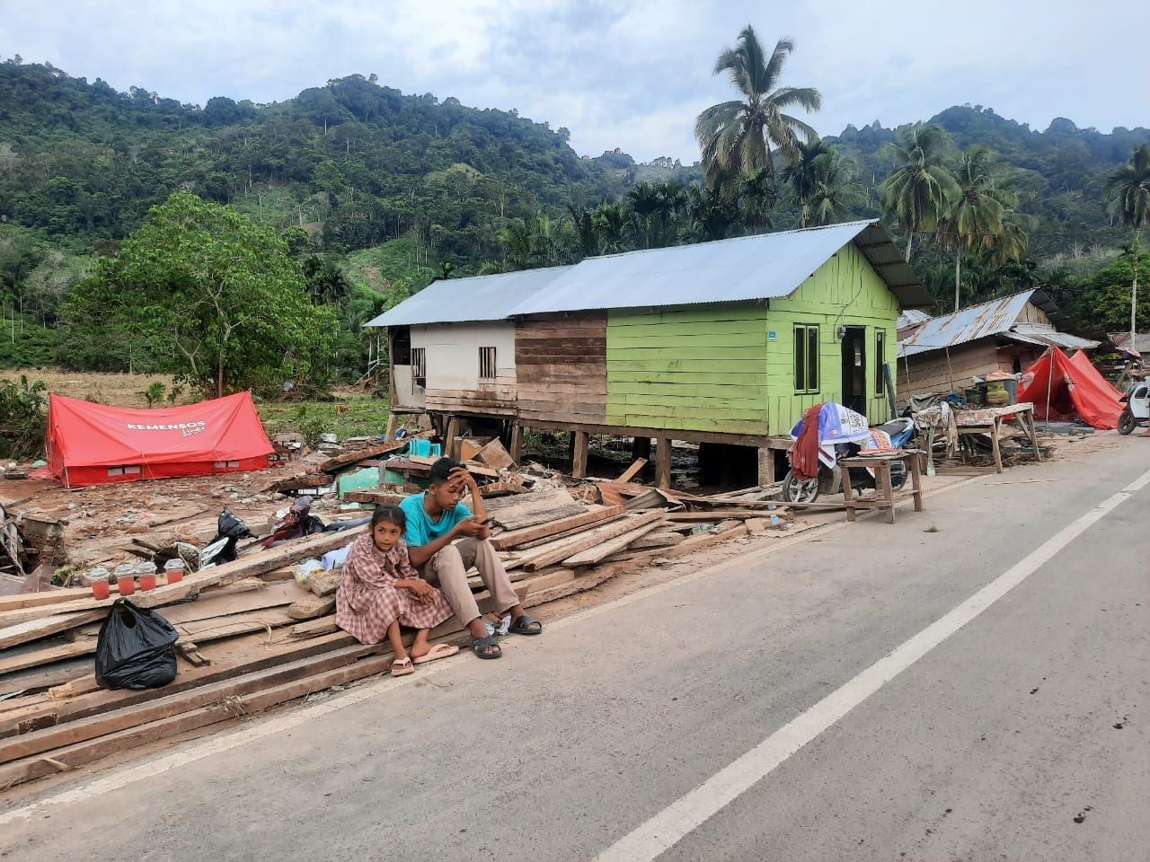 Anak dari korban banjir duduk diatas puing rumahnya yang hancur dihantam bencana alam tersebut