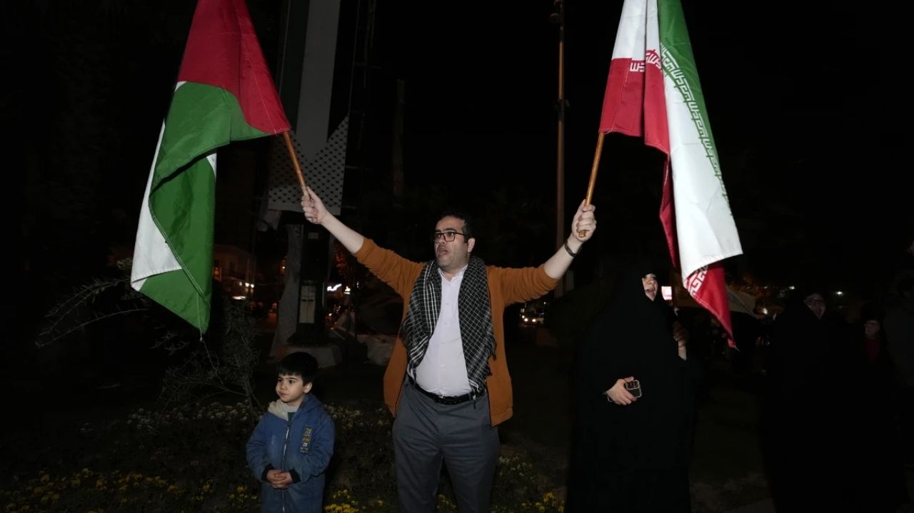 Seorang demonstran mengibarkan bendera Palestina dan Iran bersamaan.
