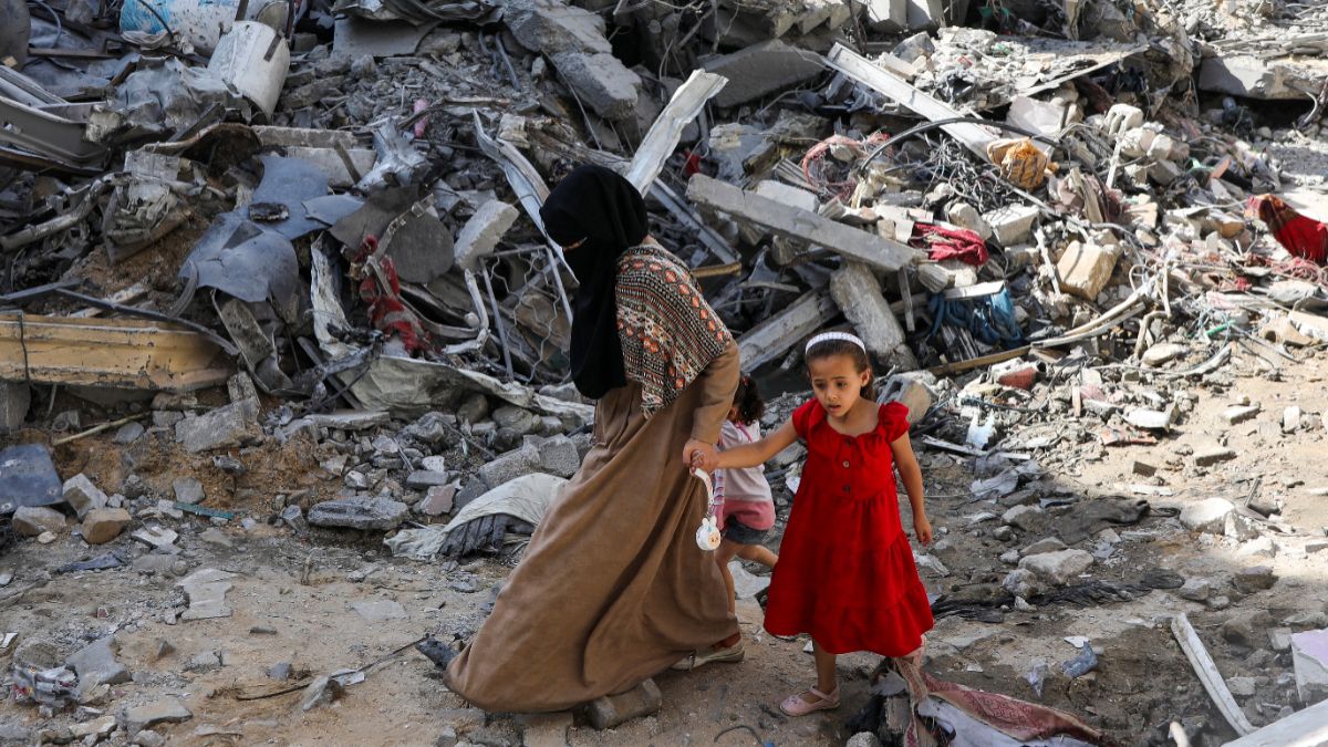 Seorang wanita dan anak-anak berjalan di antara puing-puing setelah serangan Israel.