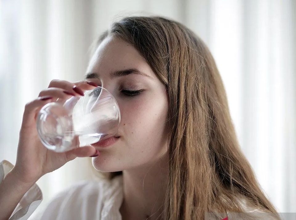 Ilustrasi - Seorang wanita sedang minum segelas air untuk menghindari dehidrasi akibat cuaca panas. 