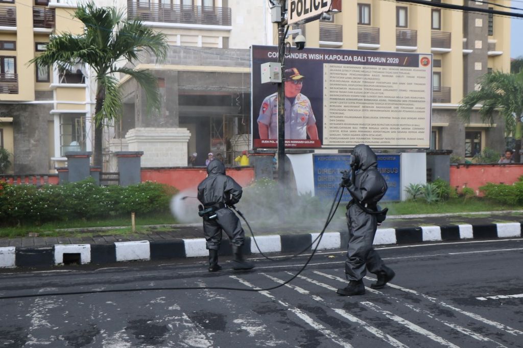 Dua anggota Brimob Polda Bali sedang melakukan penyemrotan disinfektan di depan Mapolda Bali.*/