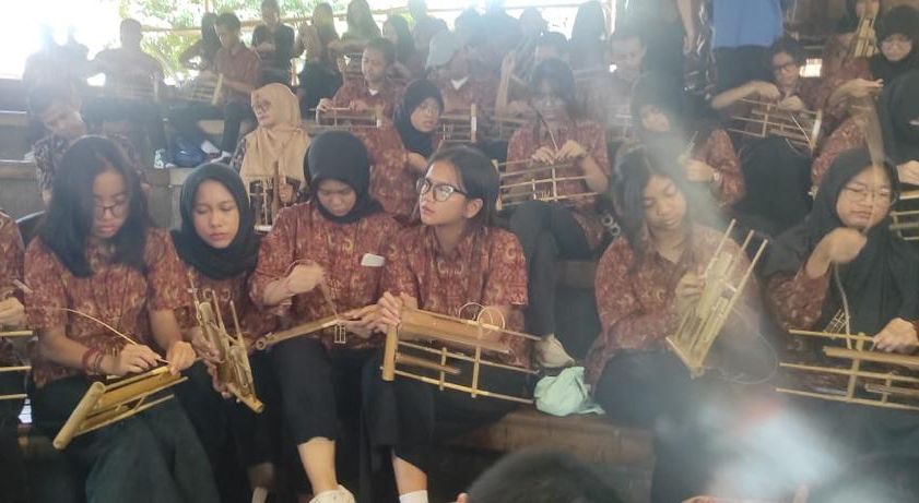 Siswa-siswi rombongan studi lapangan SMA Labschool Jakarta tengah mencoba alat musik traditionalismes Sunda, Angklung di Saung Ujo, Bandung