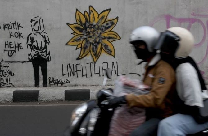 Pengendara sepeda motor berboncengan melewati mural dan grafiti di fly over Supratman Jalan Jakarta Kota Bandung.