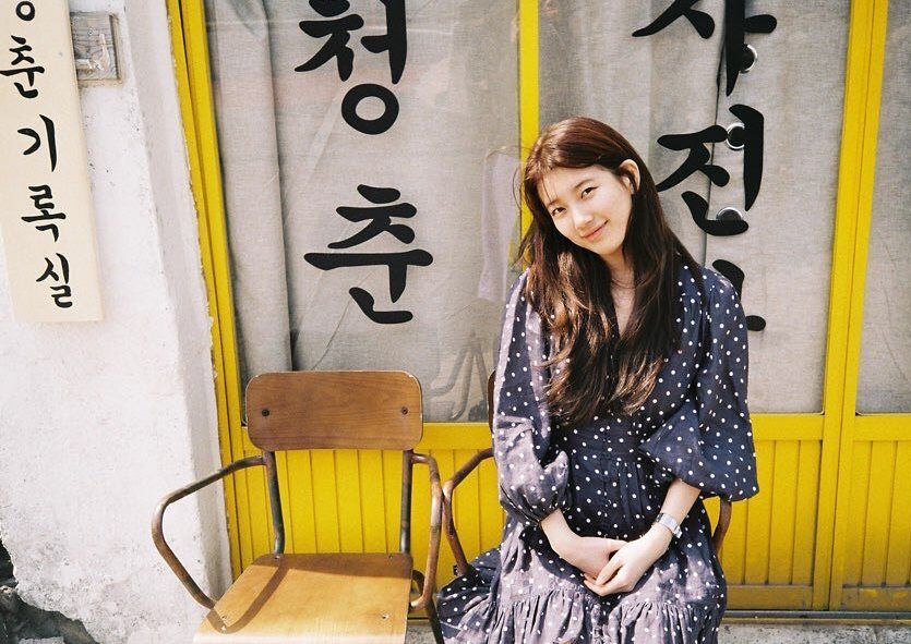 Potret Bae Suzy yang duduk di sebuah bangku depan toko