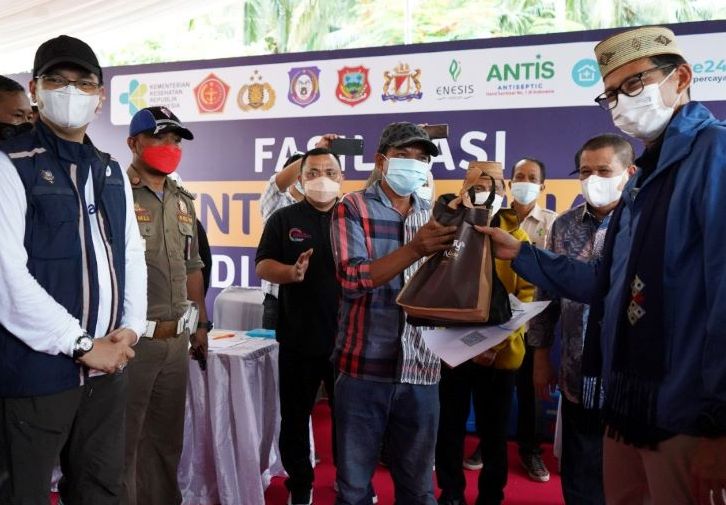 Menteri Pariwisata dan Ekonomi Kreatif Sandiaga Uno didampingi  Direktur Pengembangan Destinasi II Kemenparekraf Wawan Gunawan memberikan bingkisan pada warga yang mengikuti program vaksinasi masal.
