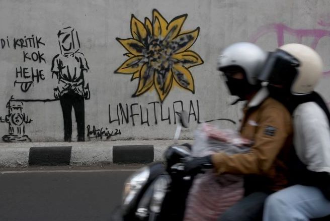 Pengendara sepeda motor melintasi mural di Jalan Jakarta Bandung.